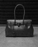 Sac Jelly Firkin Croco Obsidian noir effet croco posé au sol, vue studio devant un rideau métallique