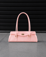 Sac baguette Jelly Firkin Cotton Candy rose poudré posé au sol, vue studio devant un rideau métallique noir